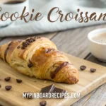 A freshly baked cookie croissant with flaky layers, placed on a wooden table with chocolate chips and a cup of coffee, featuring the title "Cookie Croissant" at the top and "MyPinBoardRecipes.com" at the bottom.
