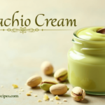 Homemade pistachio cream in a glass jar with a wooden spoon and whole pistachios scattered around, with the title 'Pistachio Cream' on top and 'MyPinBoardRecipes.com' at the bottom.